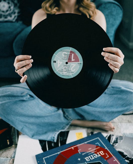 A woman sits cross-legged indoors, holding a vintage vinyl record in a cozy setting.