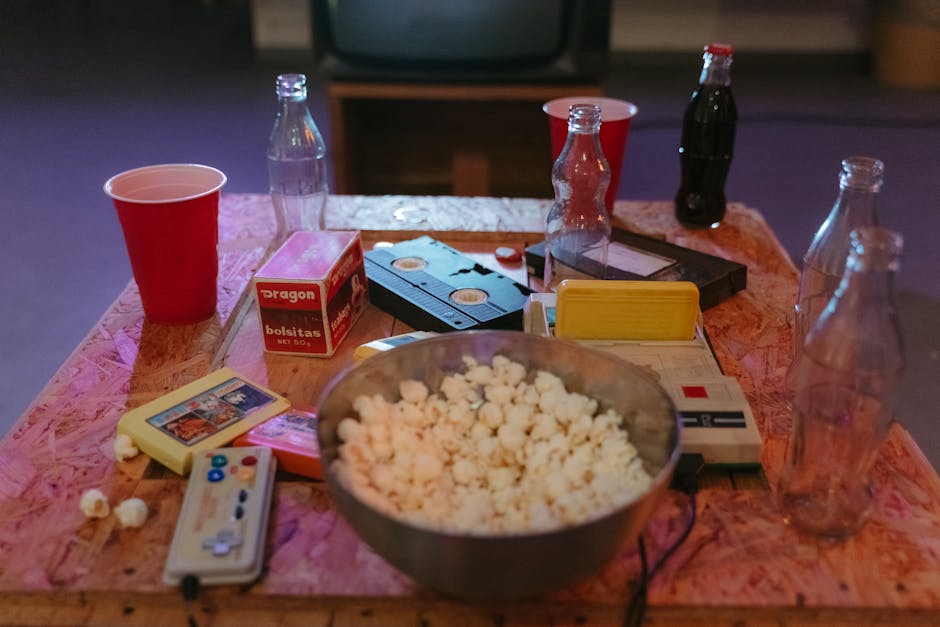 A nostalgic setup with popcorn, VHS tapes, and retro gaming consoles on a wooden table.